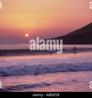 Zwei Surfer auf einer Welle Silhouette gegen den gelben Ball der untergehenden Sonne im Saunton Sands beach North Devon England Stockfoto