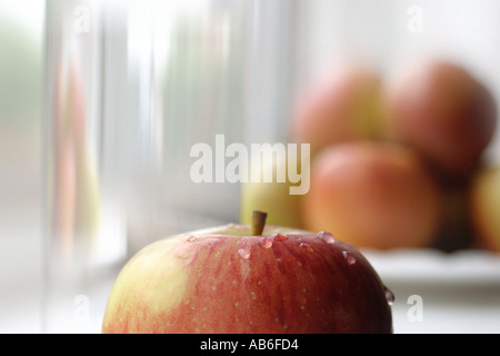 ÄPFEL AUF FENSTERBANK MIT EINEM APFEL IM VORDERGRUND MIT GLAS WASSER Stockfoto