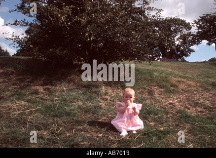 Babymädchen im rosa Kleid sitzt alleine auf einer grasbewachsenen Bank in einem park Stockfoto