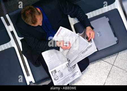 junger Geschäftsmann sitzt im Wartebereich des Flughafens, finanzielle Zeitung lesen Stockfoto