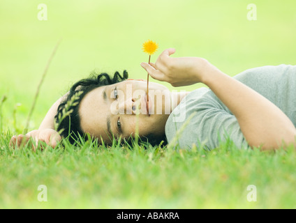 Junge Frau liegt auf dem Rasen mit Blume im Mund Stockfoto