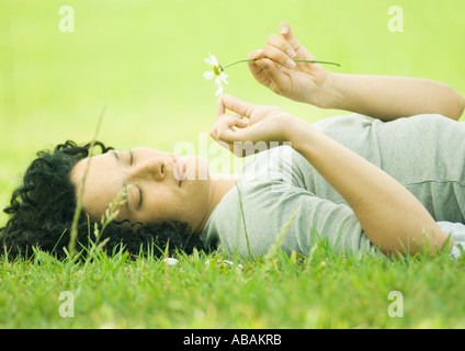 Junge Frau liegt auf dem Rasen, die Blütenblätter von Blumen pflücken Stockfoto