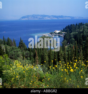 Blick auf Pinien, Zypressen und gelben Blüten zur Bucht und Fischerdorf zur albanischen Küste Kringels Korfu Griechenland Stockfoto