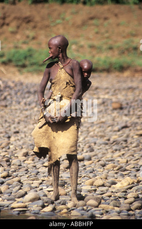 Mursi Indianerin mit traditionellen Ton Platte in Lippe, unteren Omo-Fluss in Äthiopien, Baby auf Rückseite Stockfoto