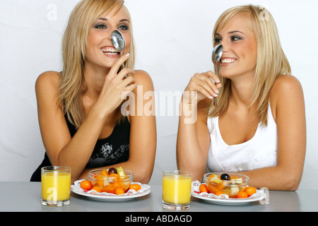 Blonde Zwillinge mit Obstsalat und Löffel Stockfoto