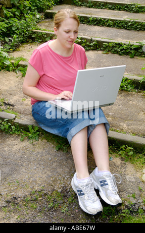 Junge Frau mit Sony Vaio Wireless-Laptop saß auf Schritte im freien gekleidet in Jeans rosa t-Shirt und Trainer UK Stockfoto