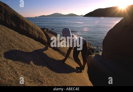 Ein weiblicher Bergsteiger durchquert auf einem abfallenden Felsen am Meer an der Küste von Hong Kong Stockfoto