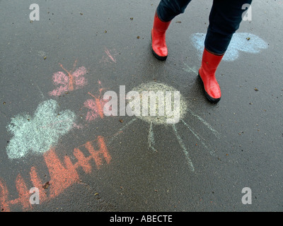 Beine einer Person Frau mit roten Gummistiefel gehen für einen Spaziergang bei Regenwetter auf nasser Fahrbahn mit schwarzen Asphaltdecke Stockfoto