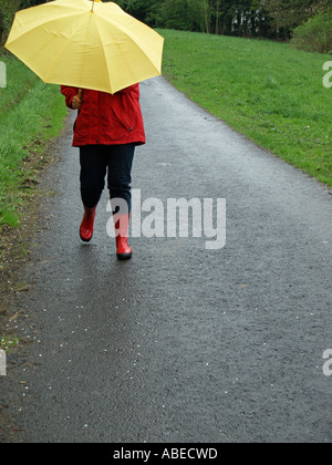 Herr Person Frau eine rote Jacke mit gelben Regenschirm bei Regenwetter spazieren gehen Stockfoto