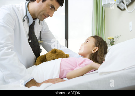 Arzt im Gespräch mit Mädchen im Krankenhausbett liegend Stockfoto