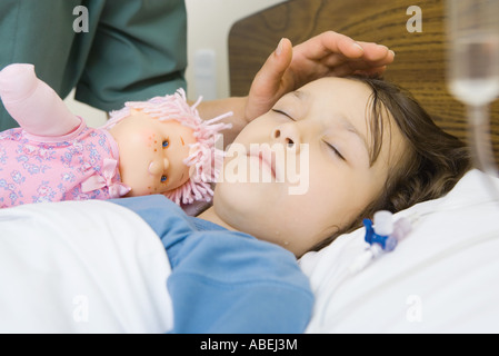 Mädchen schläft im Krankenhausbett, zarte Frauenhand gestellt über des Mädchens Stirn Stockfoto
