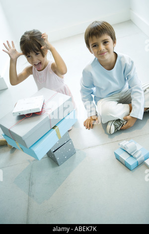 Zwei Kinder sitzen auf Boden mit Stapel Geschenke Stockfoto
