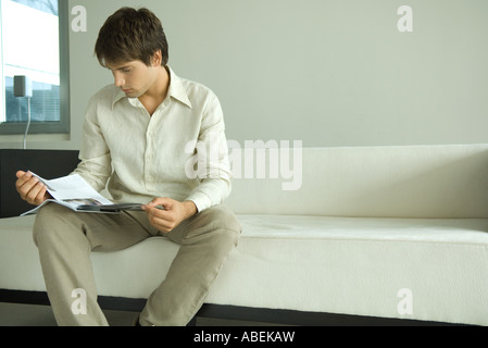 Mann sitzt auf dem Sofa lesen Magazin Stockfoto