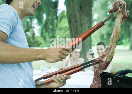 Mann hält Stück Fleisch über Grill