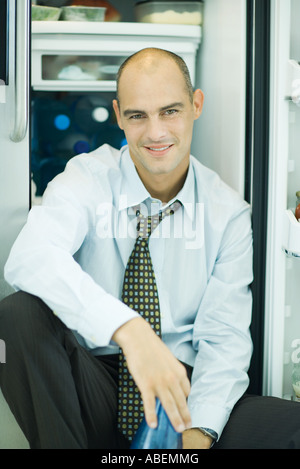 Man sitzt vor einem offenen Kühlschrank, lächelnd in die Kamera Stockfoto