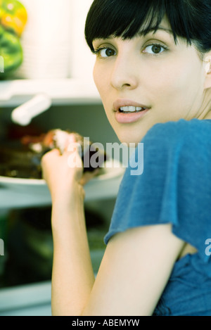 Frau, die die Kuchen aus dem Kühlschrank, über die Schulter in die Kamera schaut Stockfoto