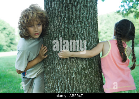 Jungen und Mädchen stehen auf beiden Seiten der Baumstamm Stockfoto