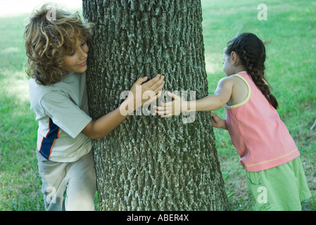 Jungen und Mädchen stehen auf beiden Seiten der Baumstamm Stockfoto