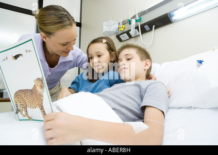 Junge im Krankenhausbett, Buch mit Mutter und Schwester Stockfoto