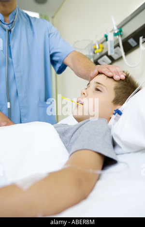 Junge liegend im Krankenbett, Arzt nehmen Temperatur und Gefühl Stirn Stockfoto