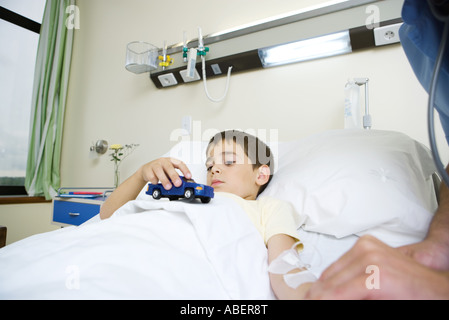 Junge im Krankenhausbett liegend, mit Spielzeug Stockfoto