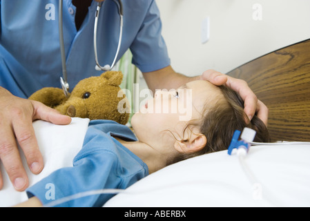 Mädchen im Krankenhausbett liegend, männliche Krankenschwester Hand auf Mädchenkopf Stockfoto