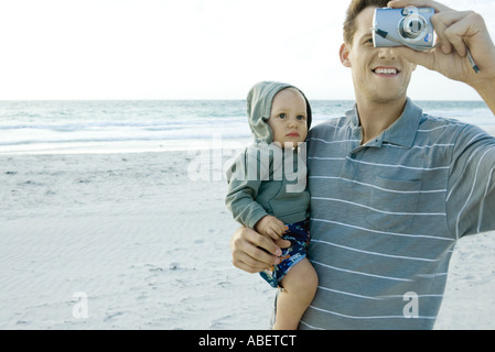 Mann hält Baby und mit Kamera am Strand Stockfoto