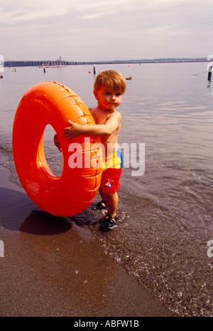 Ein drei Jahre alter Junge spielt mit einem hellen orange aufblasbares Spielzeug an einem Strand Stockfoto