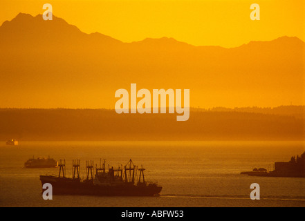 Die Sonne versinkt hinter den Olympischen Bergen die übersehen Puget Sound Elliot Bay und Frachter und Fährverkehr in Seattle Stockfoto