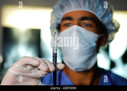 Arzt in Maske Haarnetz mit Handschuhen und Peelings mit Spritze in medizinische Klinik mit Xray Filme Stockfoto
