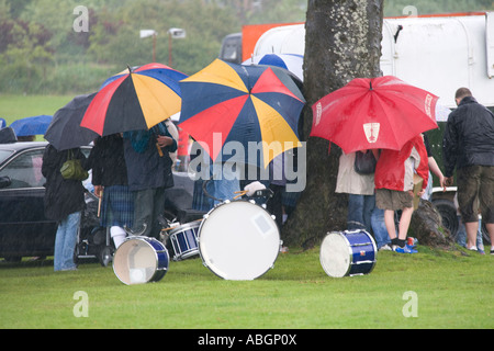 Britische Sommerzeit Schlechtwetter Regen Dudelsackkapelle nehmen Abdeckung von unten gießen unter Sonnenschirmen Scotland UK Stockfoto