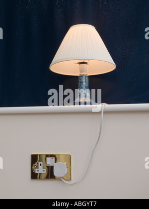 Tischleuchte mit Sahne Lampenschirm weiß Regal mit blauen Hinter in eine britische Steckdose angeschlossen. England Stockfoto
