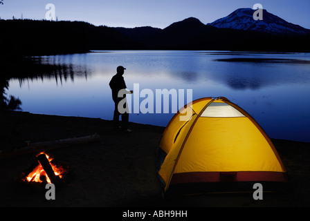 Wohnmobil mit Kaffeetasse in der Dämmerung auf Funken Seeufer mit beleuchteten Zelt und Lagerfeuer und Süden Schwester Berg Deschutes National Forest Oregon Stockfoto