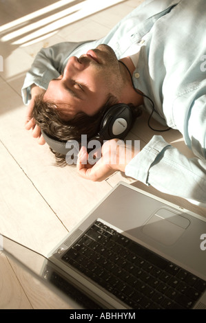 Junger Mann auf Boden liegend, Musikhören mit laptop Stockfoto