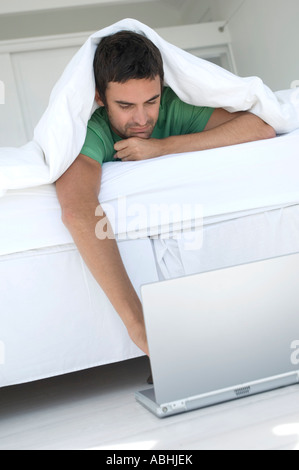 Junger Mann mit Laptop im Bett Stockfoto