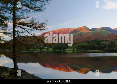 Die letzten Sonnenstrahlen im Herbst glänzen auf fernen Bergen, die sich perfekt in das Wasser des Lake Buttermere widerspiegeln Stockfoto