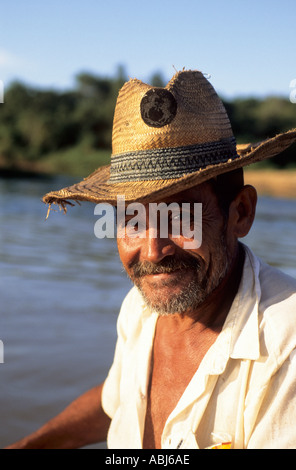 Pantanal, Bundesstaat Mato Grosso, Brasilien; Porträt von ein lächelnder Mann einen angeschlagenen Stroh Hut mit dem Fluss hinter. Stockfoto