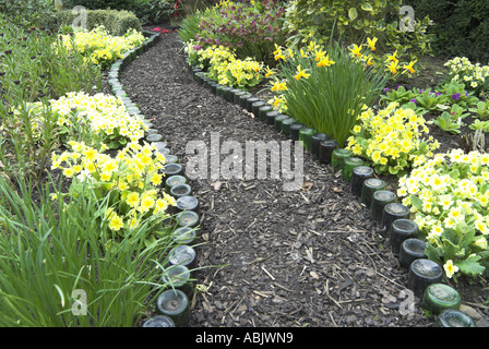 Flasche scharfkantigen Pfad in einem Frühlingsgarten mit Polyanthus und Primeln kann Norfolk Stockfoto