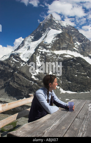 Schweiz Wallis das Matterhorn A Mädchen in ihrer Mitte der 20er Jahre genießt einen Drink und schöner Aussicht auf die Alpen von außen Schonbielhutte Stockfoto