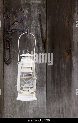 Alte renovierte weiße Kerosin-Lampe, die an einer dunklen Holztür von einer dekorativen Metallhalterung mit Vogelmotiv hängt. Stockfoto