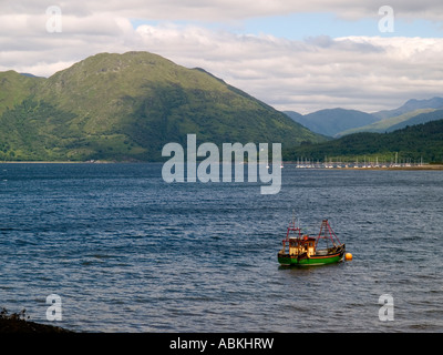 Ein kleine grüne und gelbe Fischerboot vor Anker im Loch Crerans mit einem Jachthafen und Hügeln hinter Highlands Scotland UK Stockfoto