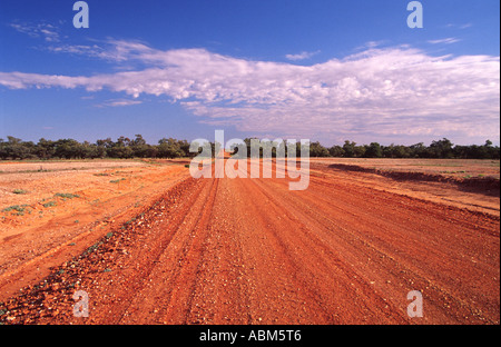 Eine lange rote Piste im australischen Outback erstreckt sich über weite rote Ebenen bis zum fernen Horizont unter blauem Himmel Stockfoto