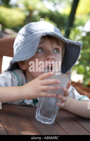 kleines Kind im Sommer tragen Diskette Sonnenhut in einem Café mit einem großen Glas kühlen gefrorenes Wasser Stockfoto