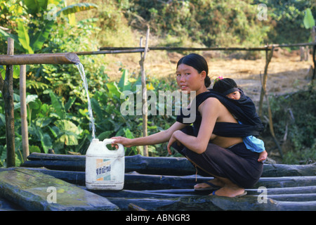 Hill Tribe Frau aus Lisu Dorf Füllung Kunststoff-Behälter mit Wasser mit Baby auf dem Rücken im Norden Thailands Stockfoto