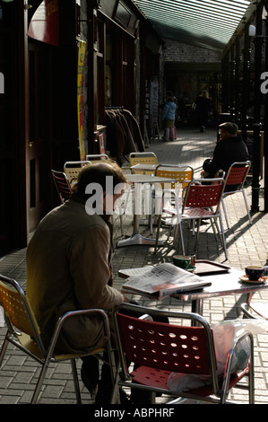 Mann allein sitzt und liest eine Zeitung in der Morgensonne, Outdoor-Pflaster Cafe, Bettws y Coed Gwynedd Nord-wales Stockfoto