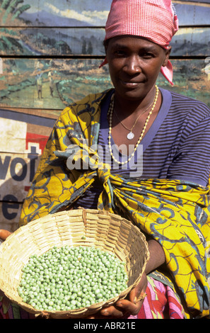 Gitega, Burundi. Frau im Markt verkaufen Erbsen und Obst vor einer bemalten Wand mit Bildern; Französische Wörter. Stockfoto