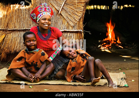 Zulu Frau im traditionellen roten Kopfschmuck heiratete Frau mit Bienenstock Kinderhütte im Hintergrund Modell freigegeben Südafrika Stockfoto