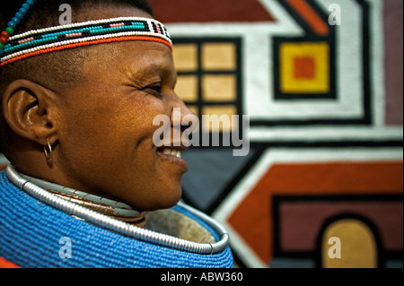 Ndebele-Frau in traditioneller Tracht mit traditionellen geometrischen Wandmalereien der Ndebele Dorf Modell freigegeben Südafrika Stockfoto