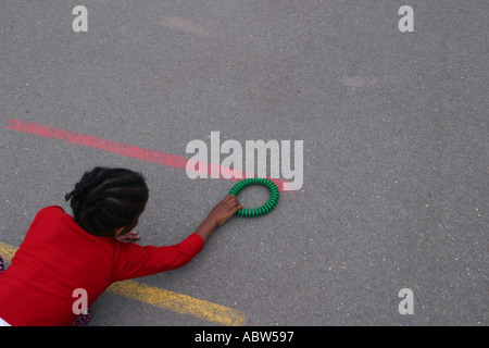 Eine Mädchen spielt mit einem kleinen Reifen in ihrer Schule Spielplatz, Betty Layward Primary School, London, Großbritannien. Stockfoto