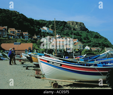 Bunt bemalte Fischerboote auf den Strand und Dorf von Runswick Bay, North York Moors Küste, North Yorkshire, England, UK. Stockfoto